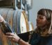 A winemaker examining a bottle beside oak barrels in an Australian winery